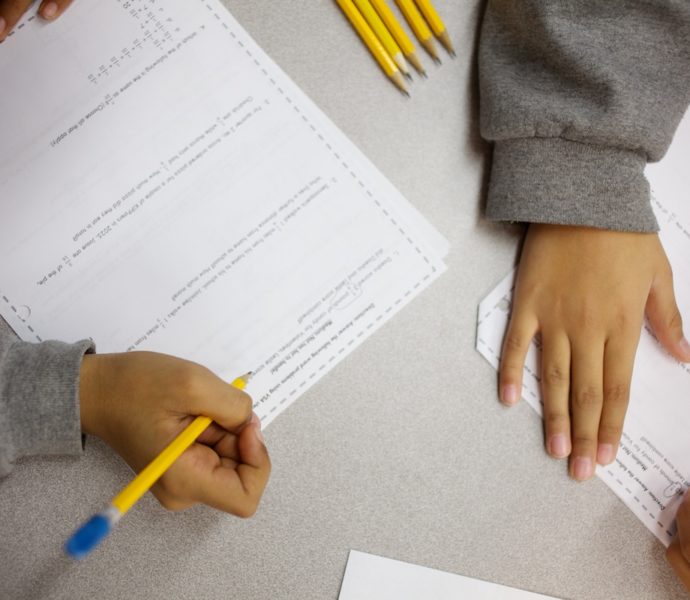 Students' hands, pencils, and paper on a desk