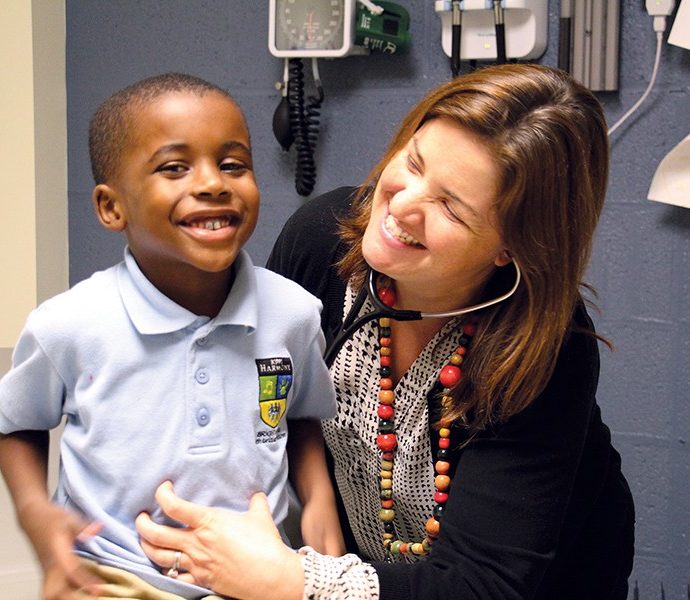 A doctor holds a stethoscope to a boy's chest, both laughing