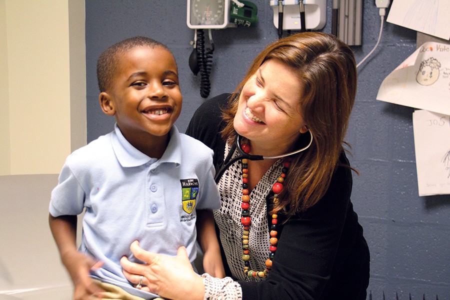 A doctor holds a stethoscope to a boy's chest, both laughing