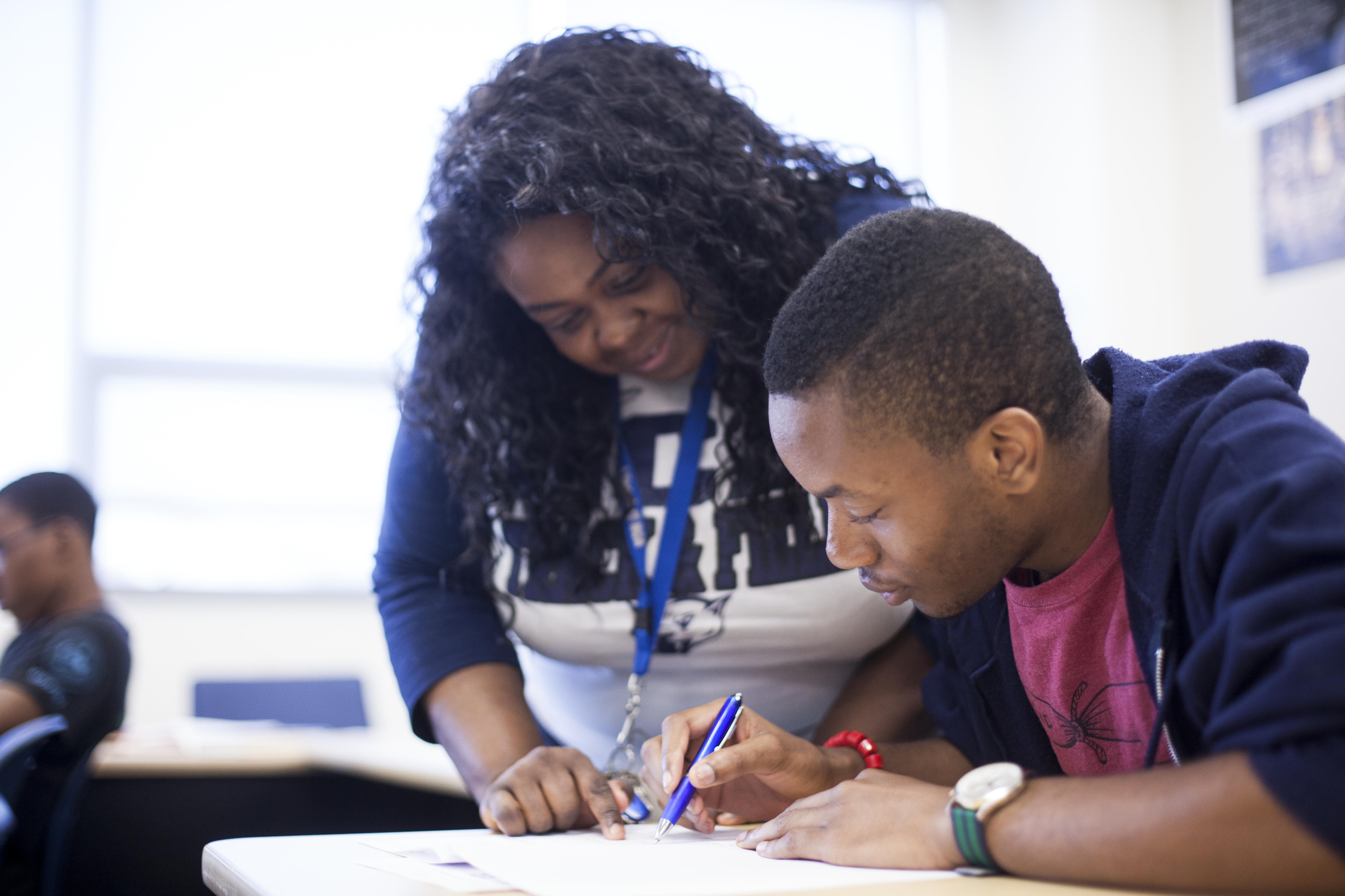 Photo shows a teacher helping a student with a task.